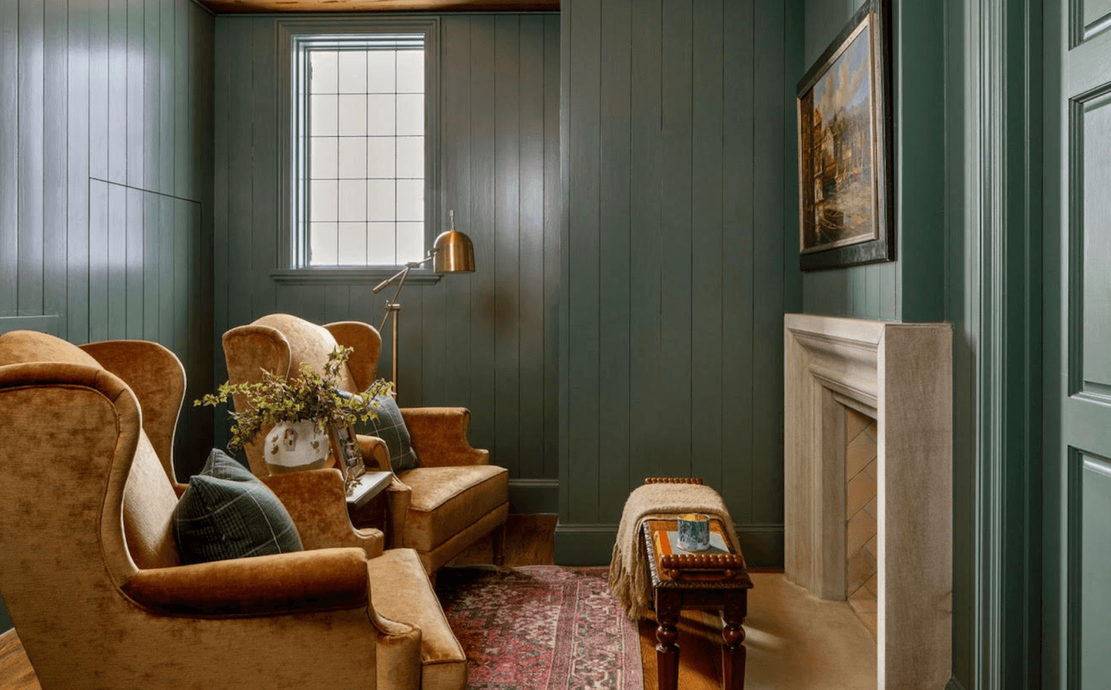 The Top Interior Designers and Architects in Birmingham - 1 A cozy room with green wood-paneled walls, a small window, two beige armchairs, a fireplace, a bench, and a vintage rug. A brass floor lamp and framed artwork are also visible—crafted with the touch of the best interior designers and architects in Birmingham.